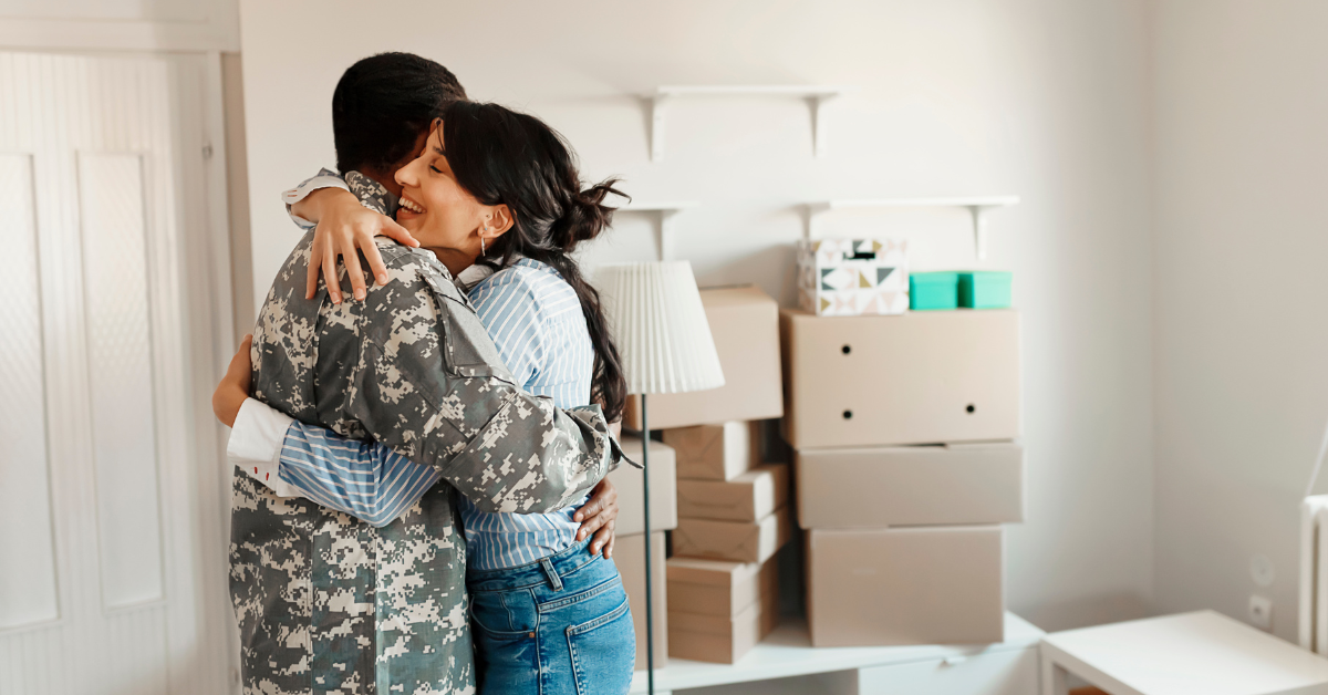 A woman and man hugging in their home, suggested they could be first-time buyers and this is their new home as they are surrounded by moving boxes.