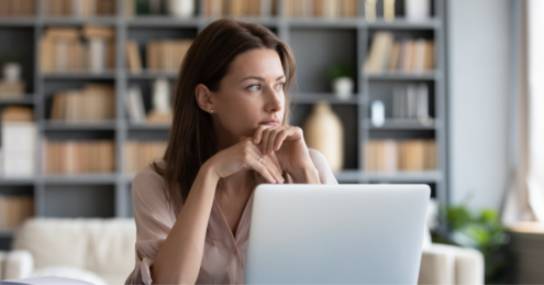 A Woman with dark hair sat at a table with her laptop open in front of her. She could be planning her next remortgage steps and planning a head for when her fixed rate mortgage ends.