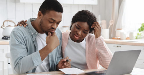 A Middle aged couple looking stressed over documents while sat at a table with their laptop. Stressed because they have left remortgaging to the last minute